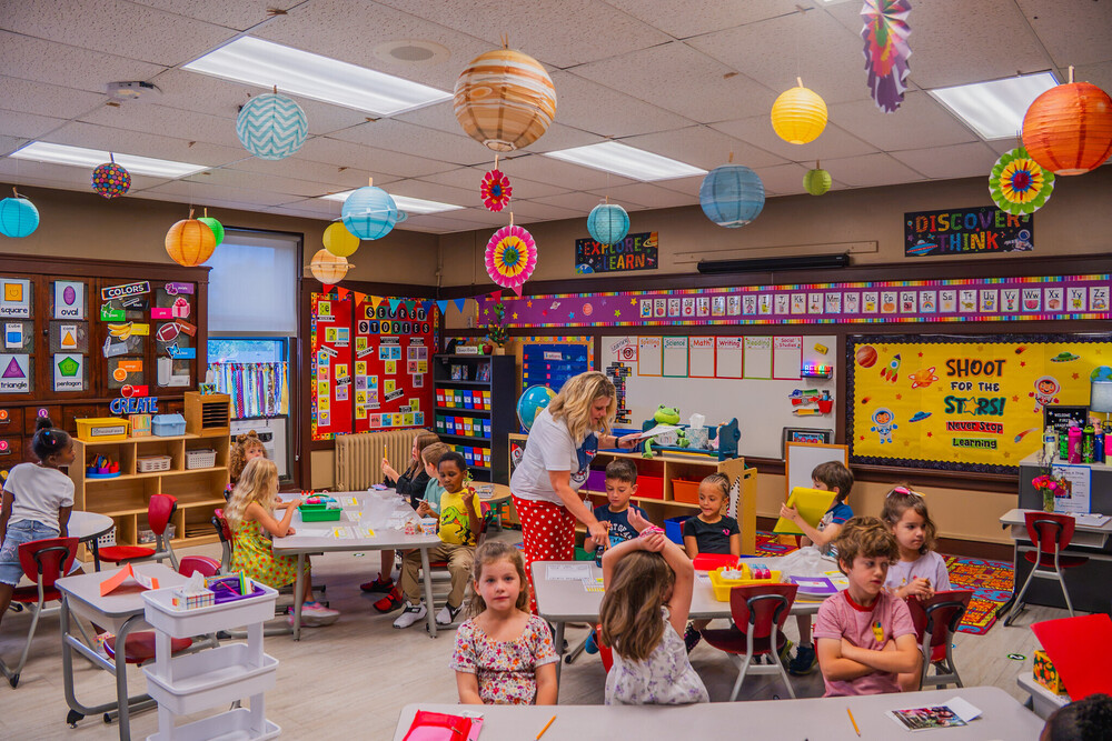 a classroom full of students sitting at desks as a teacher hands out materials