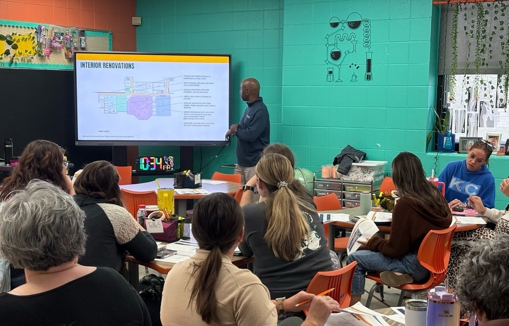 Man standing at a screen in front of an audience of KCPS staff