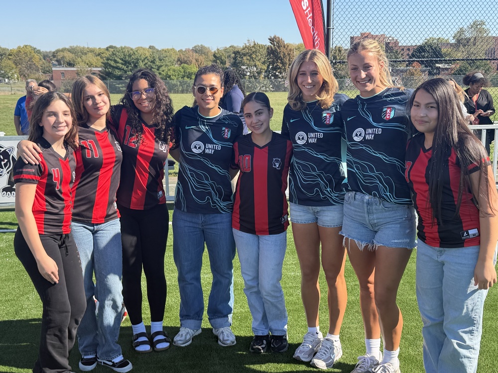 a group of women and students all wearing soccer jerseys stand in a row smiling at the camera