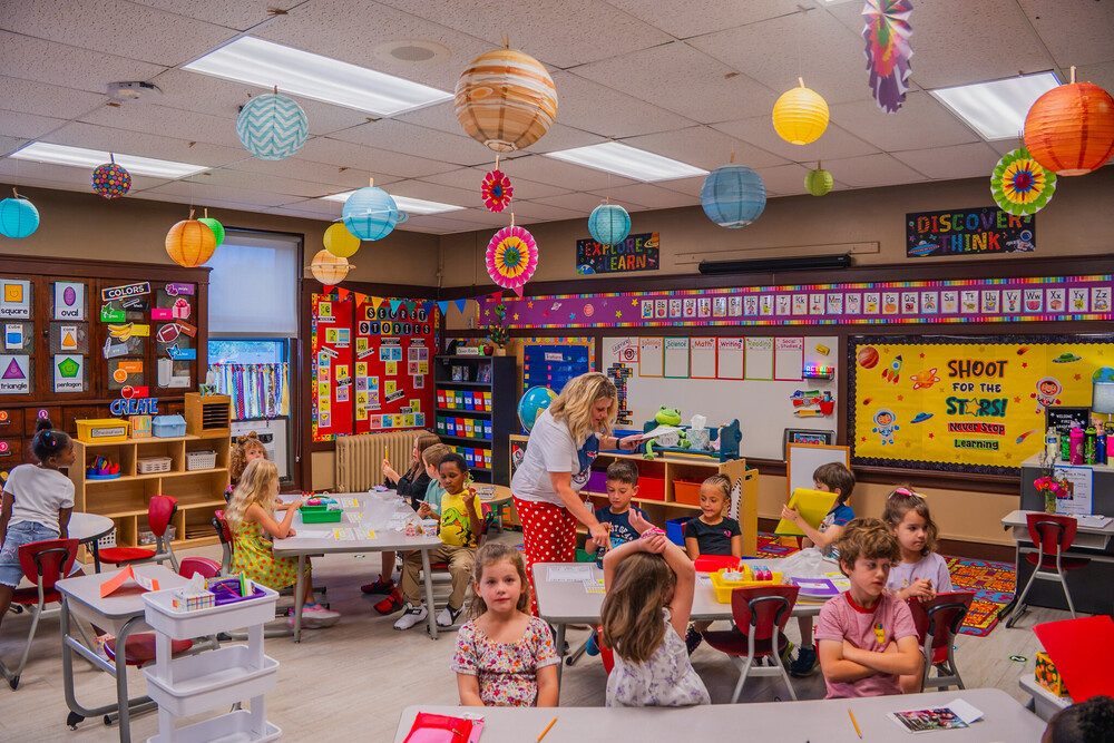 a classroom full of students sitting at desks as a teacher hands out materials