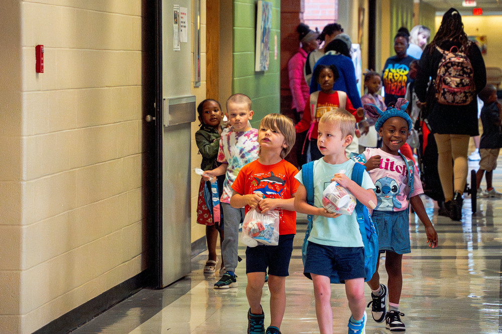 Young students walk down a school hallway with their backpacks on.