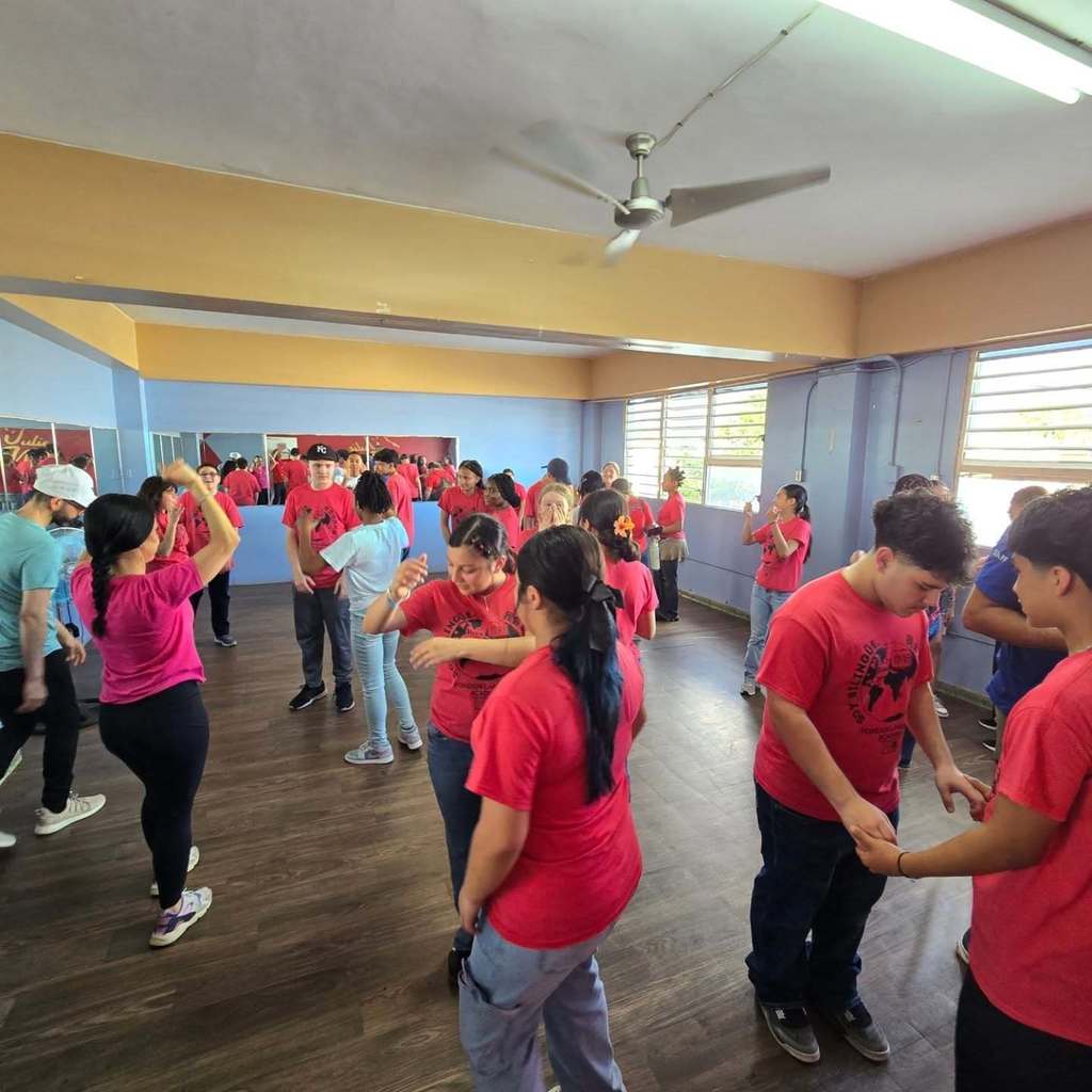 A room full of students stand in pairs learning to salsa dance.