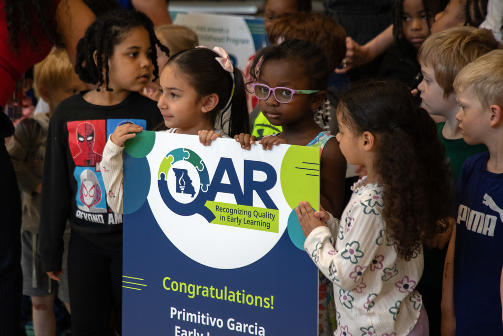 Three preschool-aged girls hold a sign congratulating Primitivo Garcia Early Learning for its high-quality programming.