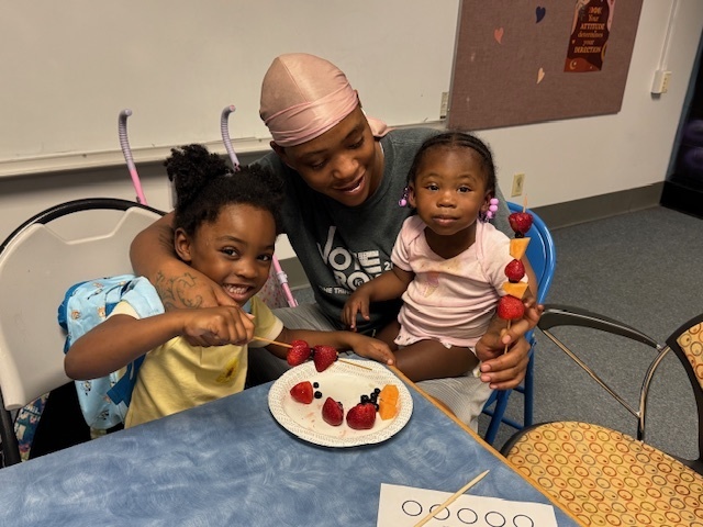 Father with two children sitting at a table eating fruit.
