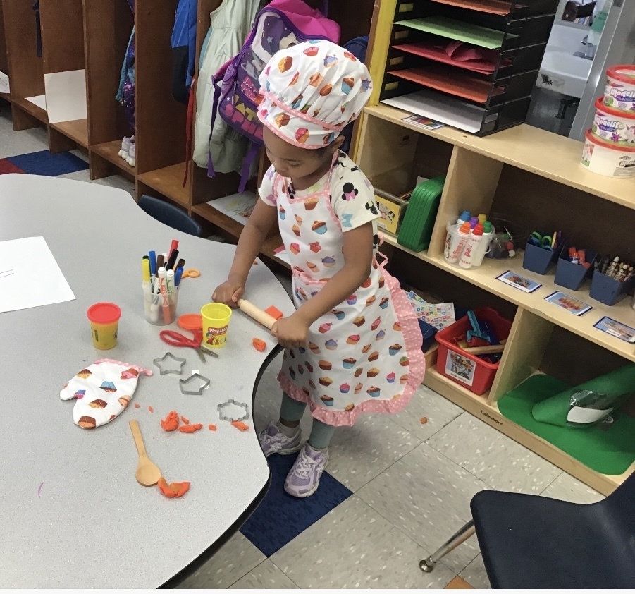 Preschool girl dressed in a chef's outfit creating food with play-doh
