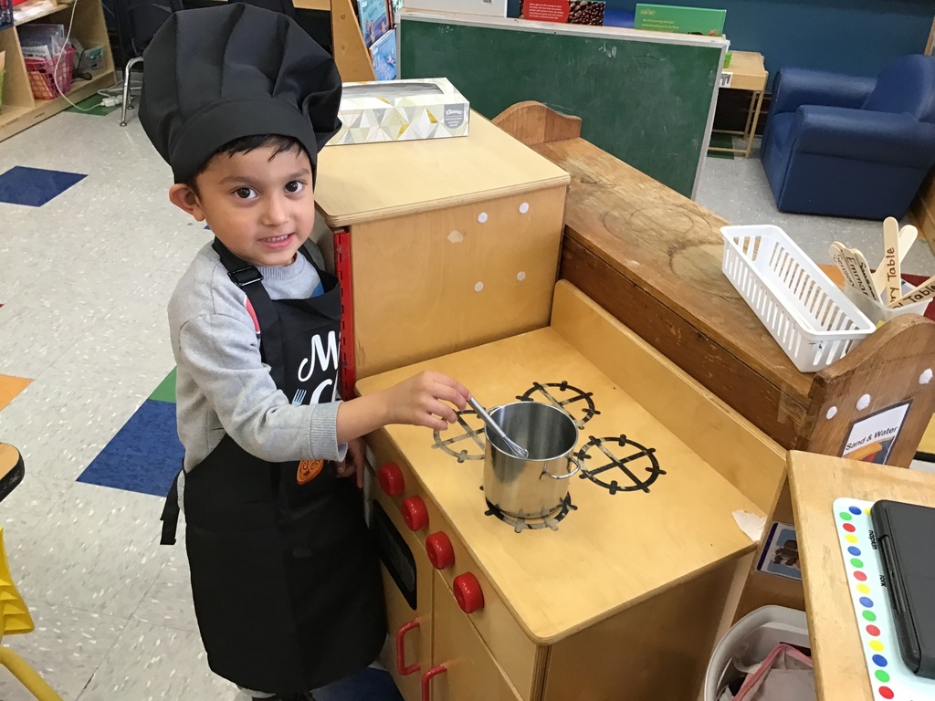 Preschool boy wearing a chef's outfit playing in the kitchen area cooking on the stove