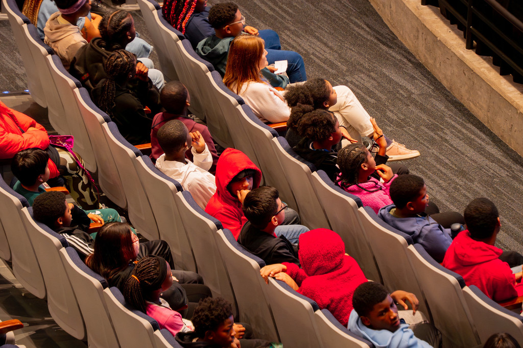 An overhead view of a crowd of people sitting in school auditorium seats