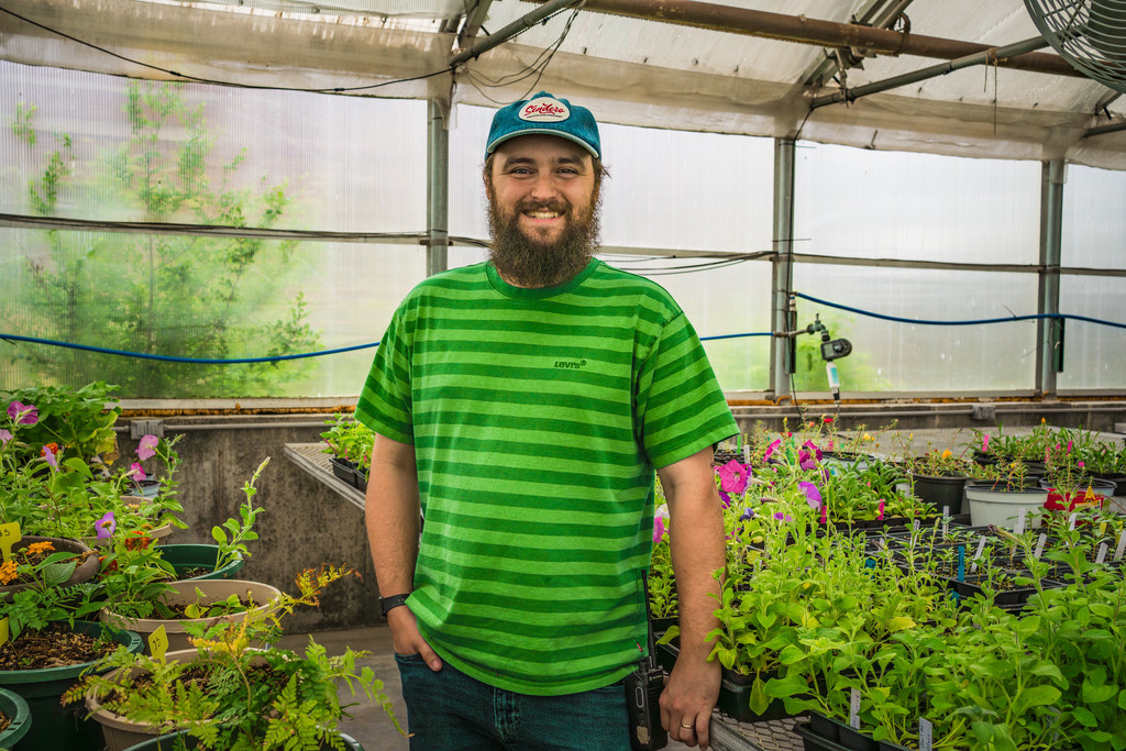 A man wearing a green striped t-shirt and standing in a greenhouse surrounded by plants