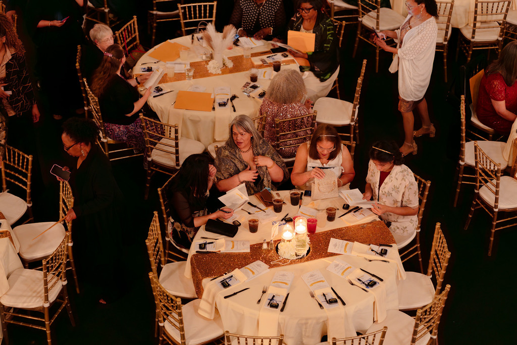 An overview of round tables set for a formal event with people sitting and walking through the space