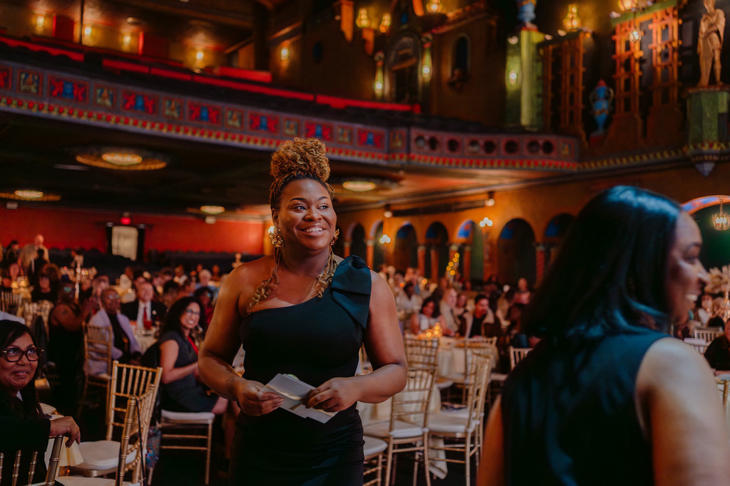 A woman in a formal black dress walks toward a stage