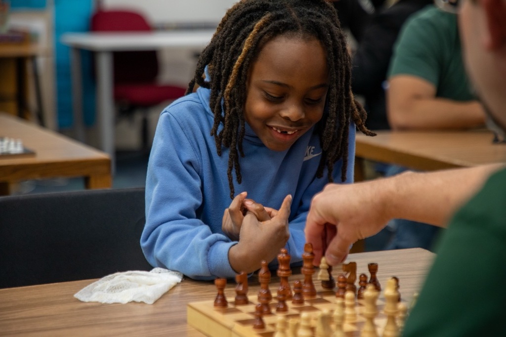 A young student smiles as he watches his chess opponent make a move