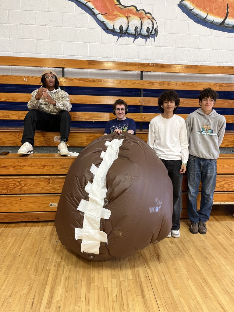 Students stand behind a handmade, football-shaped inflatable project