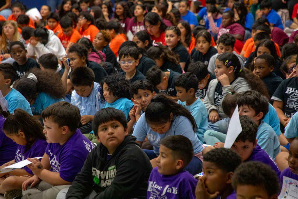 A crowd of students sit on the floor of a gym for a leadership assembly