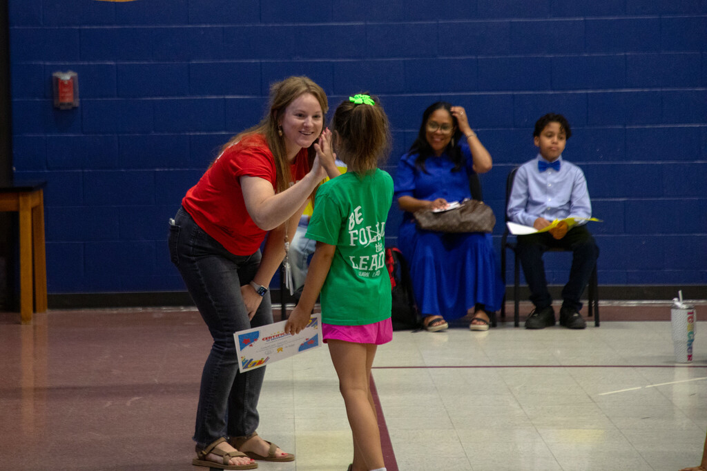 A teacher high fives a young student who just received a certificate of academic achievement