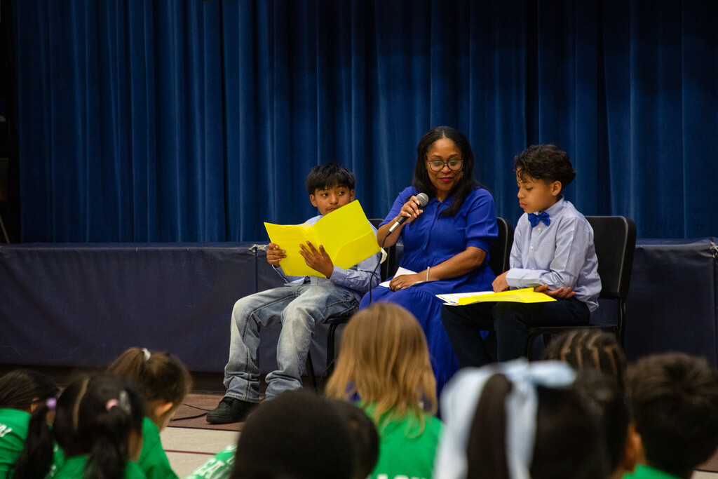 Superintendent Dr. Collier sits at the front of a crowd of students as two students sitting next to her ask her questions