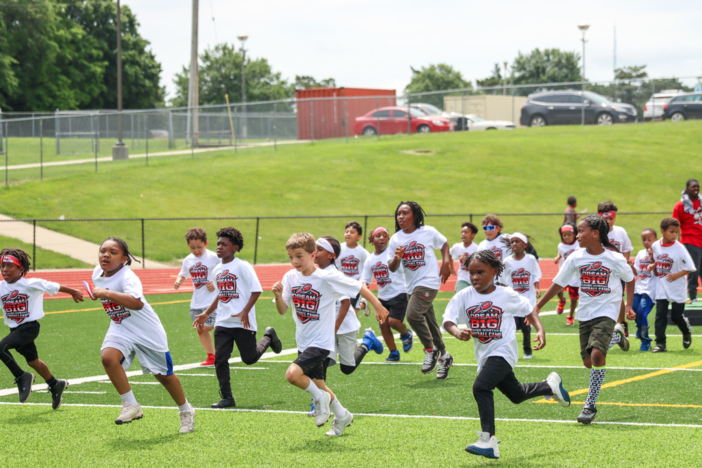 a group of children of all ages run across a football field wearing matching "Dream Big" t-shirts