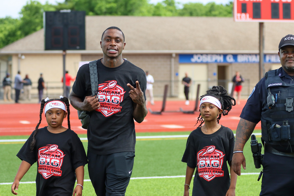 Chiefs wide reciever Xavier Worthy walks with two young students at his side as he enters a football field for his free camp