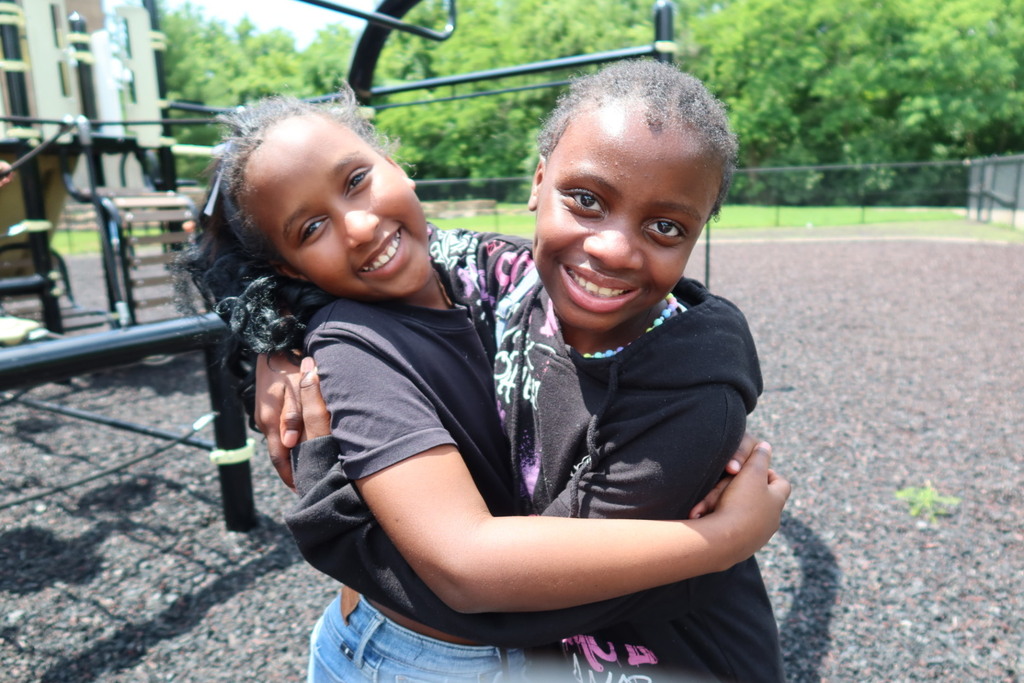 Two students hug each other on a playground while looking at the camera
