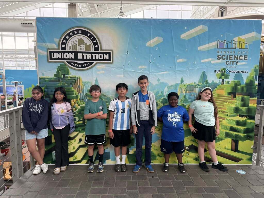 Students stand in front of a science city backdrop smiling for a photo