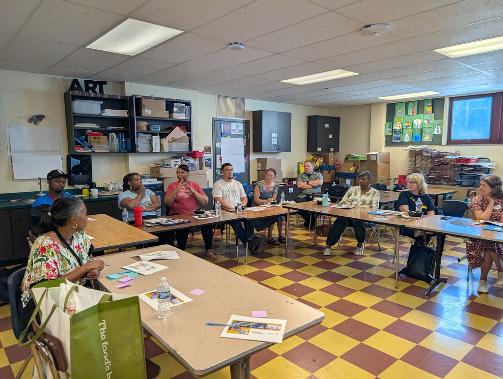 A room of adults sit at tables that are set up in a "u" shape to discuss pre-construction updates on the Woodland/Whittier Empowerment campus