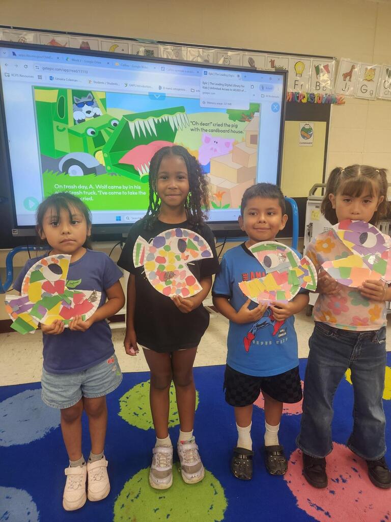 First grade students hold up the art projects they made using recycled materials