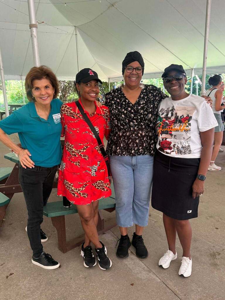 Four women stand with their arms around each other smiling at the camera