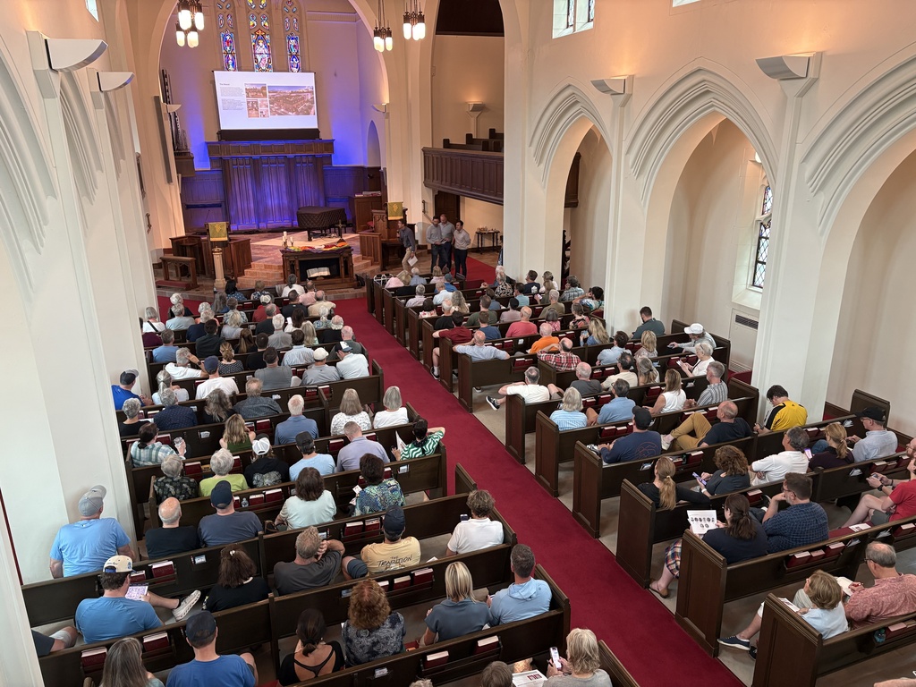 An overhead view of a church with pews packed full of community members learning about developers' plans for the Bryant School site