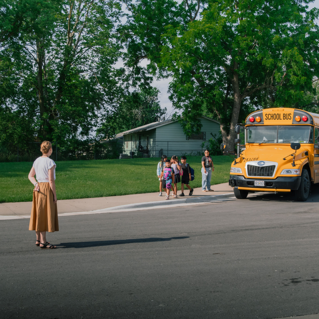 A woman stands waiting for students as they exit a school bus