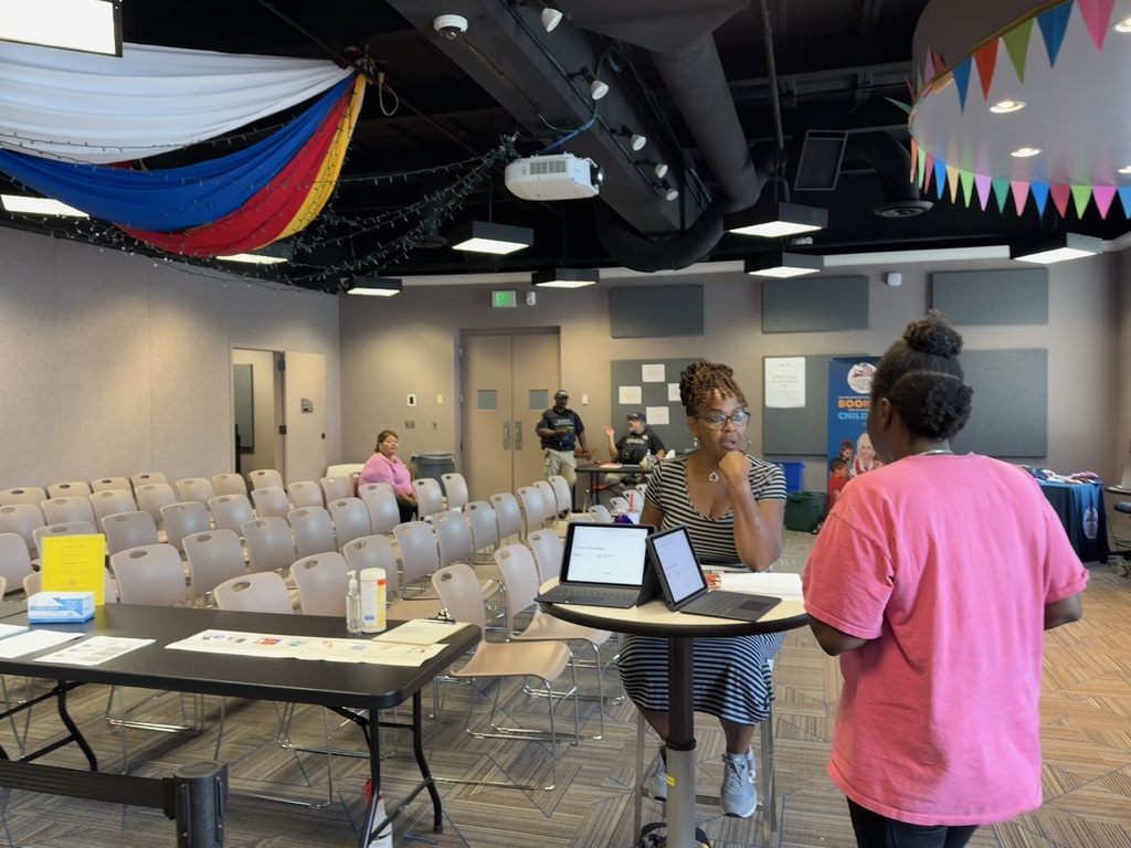 A woman in a bright pink t-shirt talks to a woman who is sitting at a table facing her