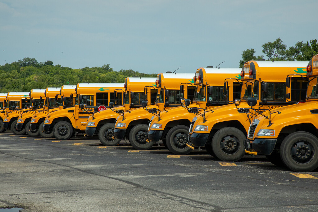 an unbroken row of schoolbuses parked in a line stretch across the photo
