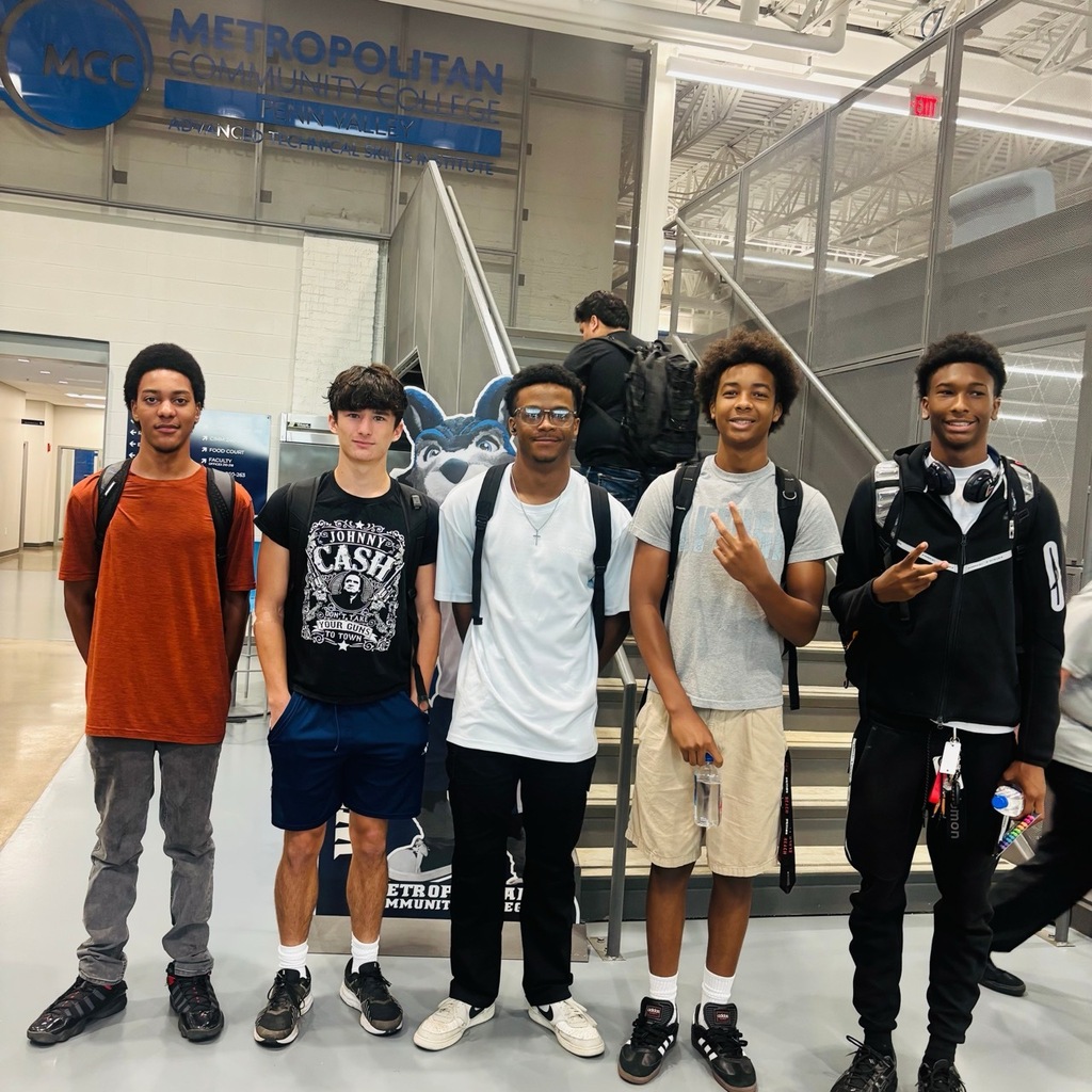 Five high school boys with backpacks stand in a line smiling at the camera. A sign for metropolitan community college is visible on the wall behind them