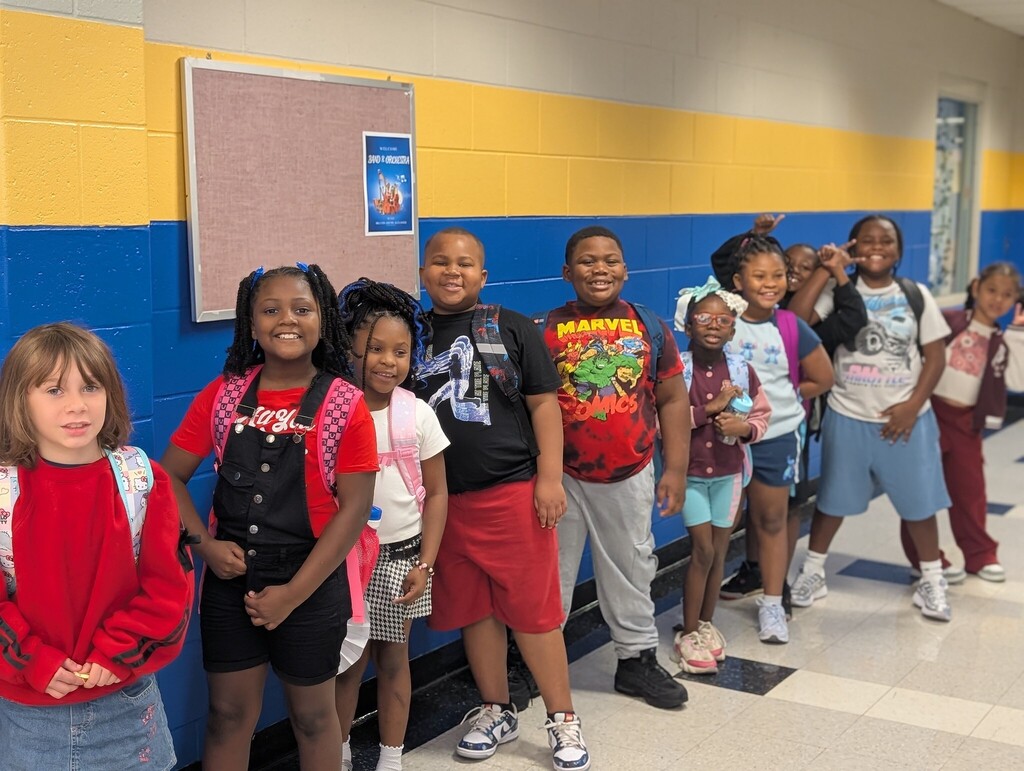 young students stand lined up along a hallway wearing their backpacks