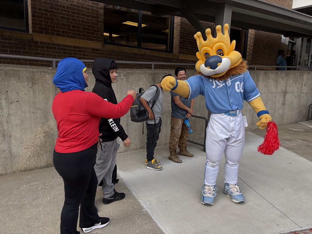 The royals mascot sluggerrr fist bumps an adult woman wearing a long-sleeved shirt and hijab