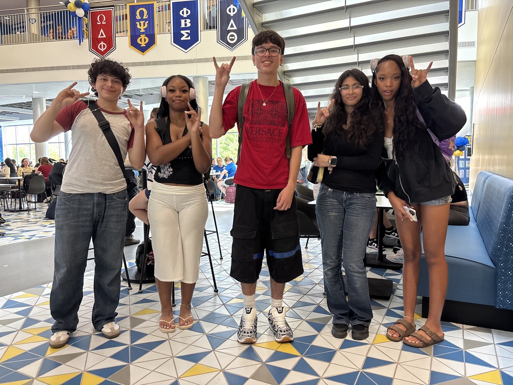 three young women and two young men stand together posing for the camera with their pinky and pointer fingers pointed upright and their thumbs and two middle fingers joined to make the "roo" handshape