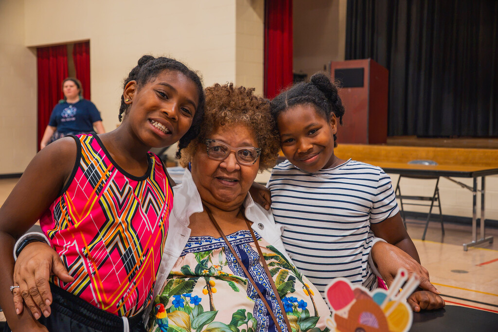 two young girls stand on either side of their grandmother as all three smile at the camera