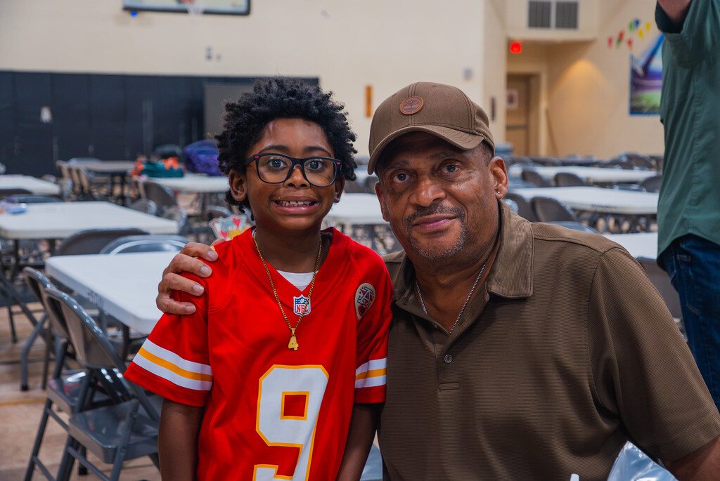 a young boy in a chiefs #9 jersey stands next to his grandfather who is kneeling next to him with his arm around him