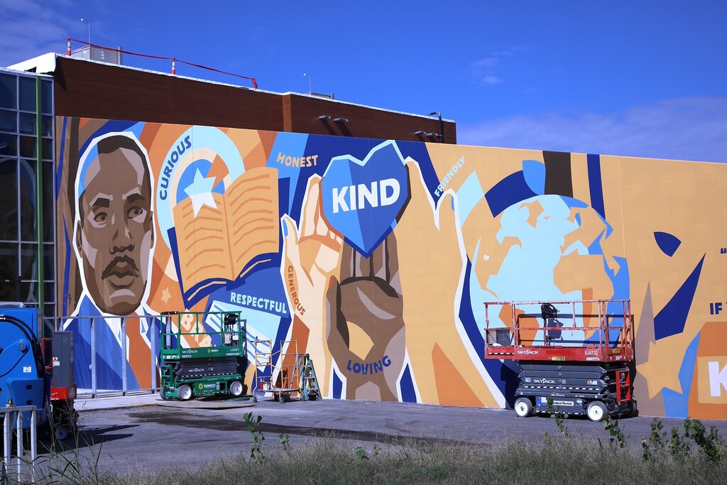 a mural on the side of a building featuring martin luther king jr. on the left side, hands lifting up a heart that has the word "kind" in the middle, and a globe to the right