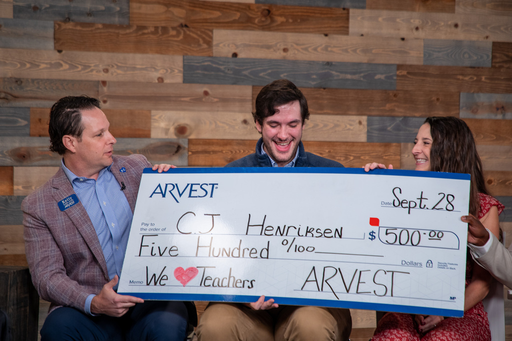a man holds a large check with another man and woman sitting on either side of him