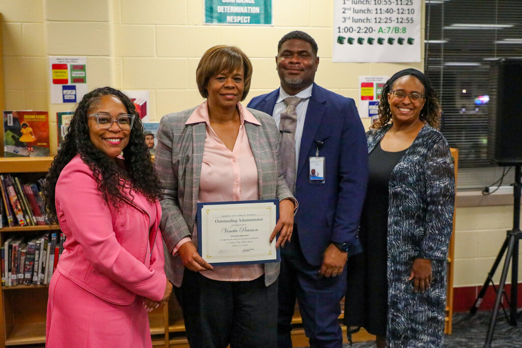 a group of four adults stand smiling at the camera as the recipient of a superintendent award holds their certificate