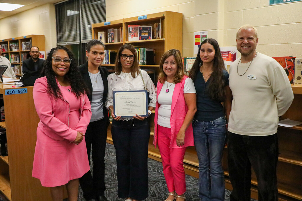 a group of adults stand smiling at the camera as the recipient of a superintendent award holds their certificate