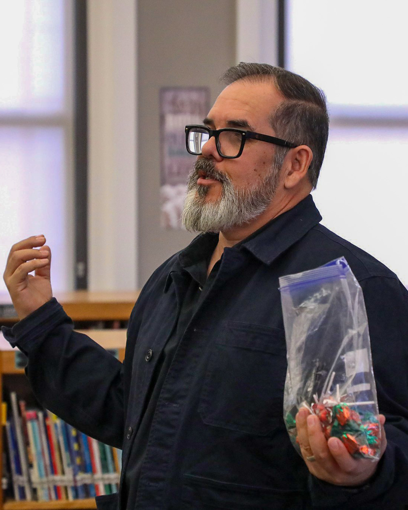 a man holding a book talks to a crowd off camera