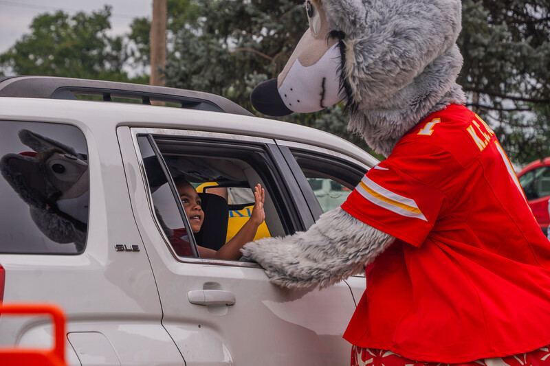 Chiefs mascot KC Wolf stands outside of a car while a child inside smiles and waves at him