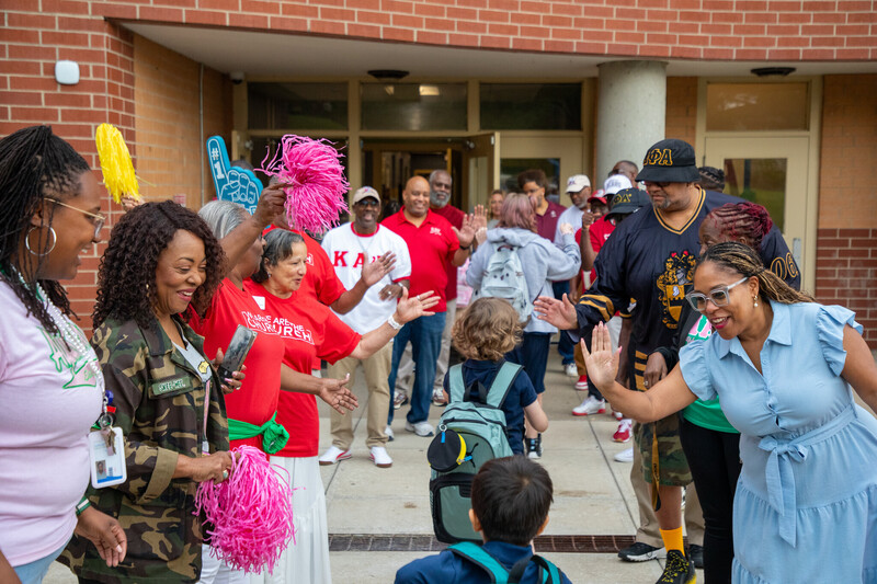 two lines of adults stand waiting to high five the students walking between them toward a school building