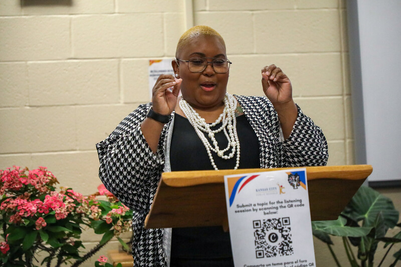 a woman stands behind a podium addressing an audience using American Sign Language