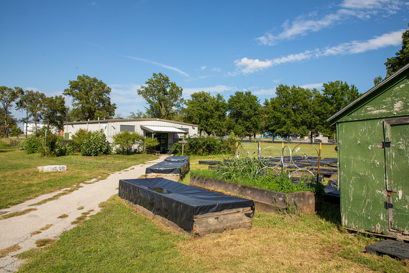 a landscape view of an agriculture area with empty plant beds, trees, and a building in the distance