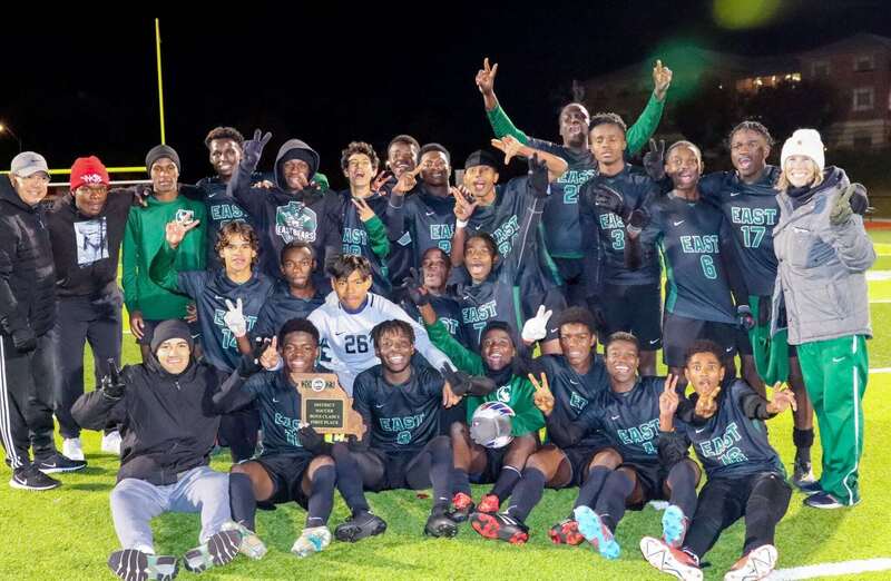 the east high school soccer team gathers with their state championship trophy smiling at the camera