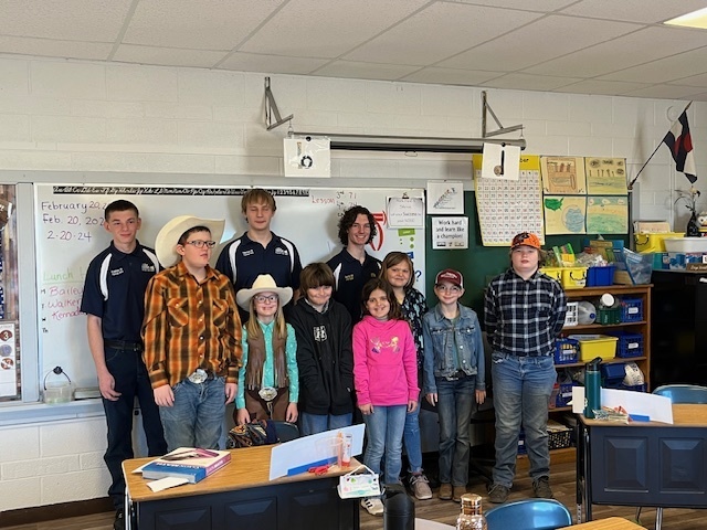 FFA members and 2nd-5th grade students pose in an elementary classroom.