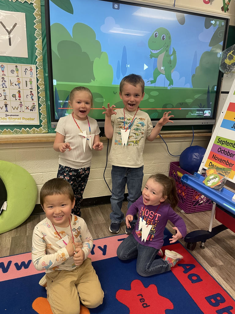 Preschoolers pose as T-rex dinos with teeth necklaces.