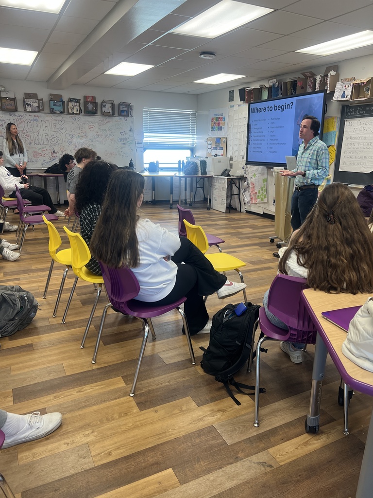students sitting in class listening to a speaker who is standing