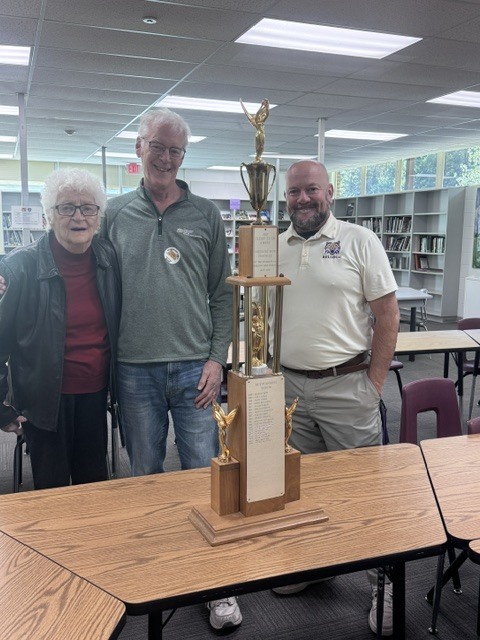 a woman and two men posing in a library with a trophy